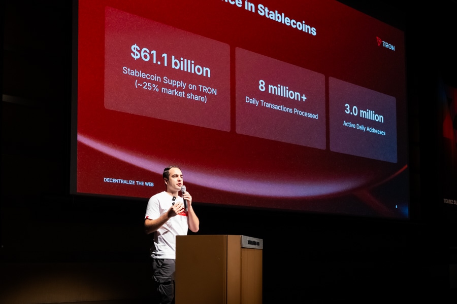マイクを持ち講演中の男性の背後に、TRONのステーブルコインに関する市場シェア61.1ビリオンドル、日次取引800万件以上、アクティブデイリーアドレス300万の統計が映し出されたスクリーン。