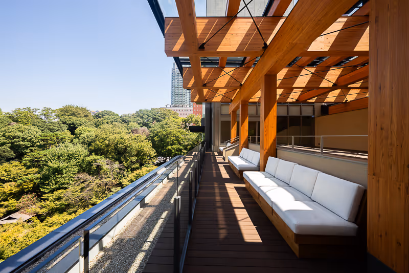 木製の屋根と白いソファが並ぶ、緑豊かな景色を望む屋外バルコニー。